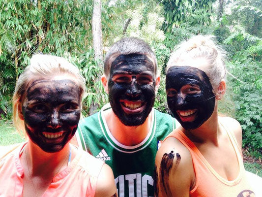 A group of three friends laughing and smiling while wearing a dark mud mask treatment.