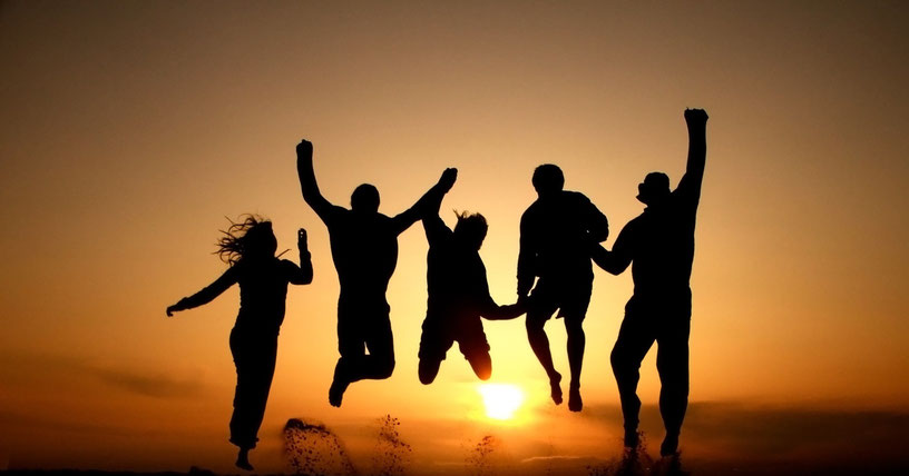 A silhouette of five friends jumping in the air against a bright sunset.