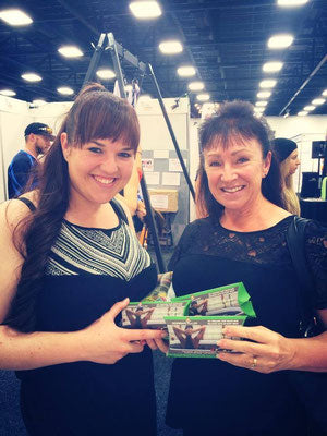 Two smiling women holding product samples at an event, representing happy customers and brand trust.