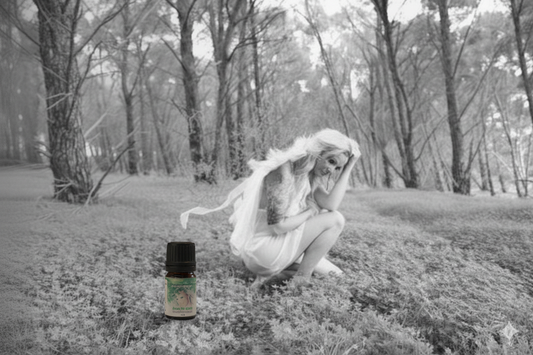 Person in a white dress sitting on grass with a bottle of essential oil in the foreground.