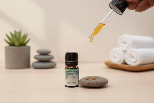 A hand holding a dropper of yellow oil over a stone, with a bottle of essential oil nearby.