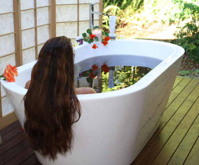 A woman with long dark hair relaxing in an outdoor Moor Mud bath in a lush garden setting.